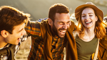Gruppo di amici abbracciati e sorridenti passaggiano in mezzo alla natura.